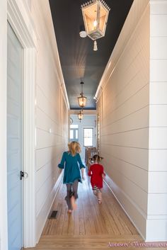 two children are walking down the hallway in front of an open door and light fixture