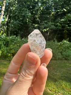 a person holding up a piece of clear rock in their hand with trees in the background