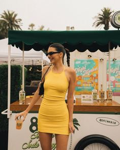 a woman in a short yellow dress is holding a drink and posing for the camera