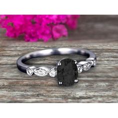 an oval shaped black diamond ring with three diamonds on the band and a flower in the background