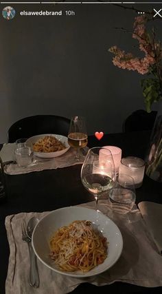 the table is set with two plates of spaghetti and wine glasses on it, along with candles