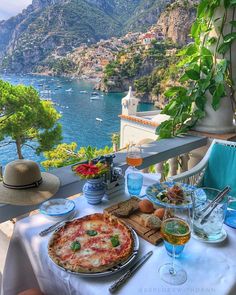 a table with pizza and drinks on it overlooking the water's edge in italy