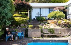 a man sitting at a table next to a swimming pool in front of a house