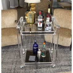 a clear bar cart with liquor bottles and glasses on the top, in front of two chairs