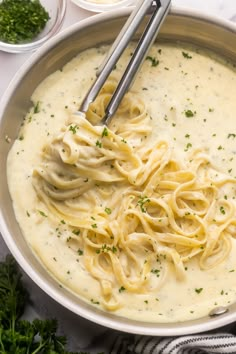 a bowl filled with pasta and sauce on top of a white table next to bowls of parsley