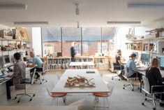 people sitting at desks in an office with bookshelves on the walls and windows