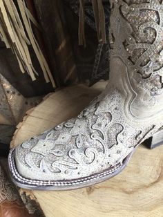 a pair of white cowboy boots sitting on top of a piece of wood