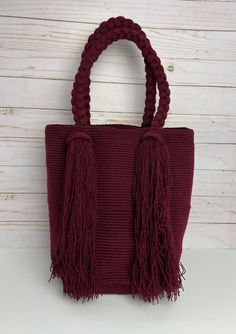 "This elegant Burgundy top handle bag is perfect for traveling, going to the beach, or just for everyday life. This hand-knit bag was 100% hand knit by Wayuu Women. The Wayuu women are not only the center of the family but also cultural leaders, and one of the most significant aspects of their culture is the art of crocheting.  The bag represents about a week worth of work for a Wayuu woman and is the primary source of income for this community. The bags are a work of art and a unique piece that Red Handheld Bags With Braided Handles, Elegant Red Woven Bag, Luxury Red Handwoven Bags, Red Eco-friendly Shoulder Bag With Braided Handles, Eco-friendly Red Handwoven Bag, Hand Knit Bag, Handwoven Bag, Trendy Shoulder Bag, Burgundy Top