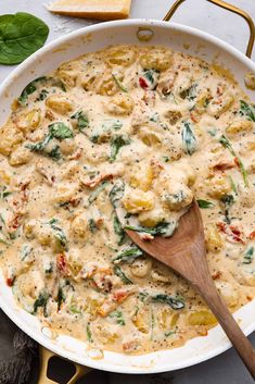 a casserole dish with spinach, cheese and bread on the side next to a wooden spoon