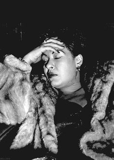 a black and white photo of a woman with her hands on her head while she is wearing a fur coat