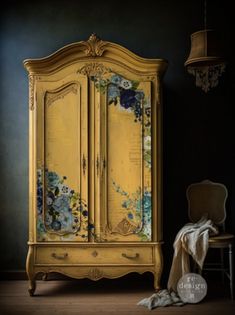 an old yellow armoire with flowers painted on it and a chair next to it