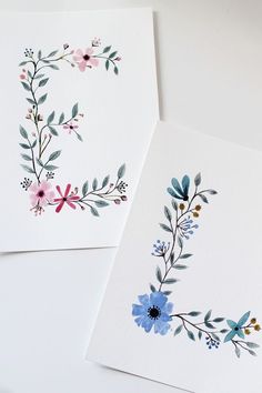 two cards with watercolor flowers and the letter e painted on them are laying next to each other