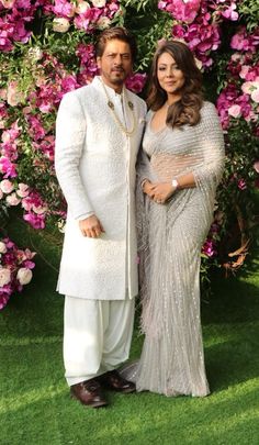 two people standing next to each other in front of pink flowers and greenery on the grass