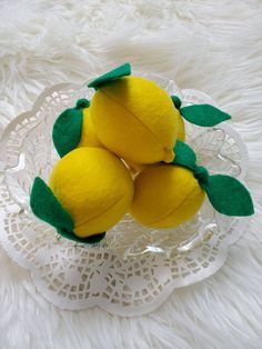 three lemons sitting in a glass bowl on a lace doily with green leaves