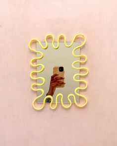 a hand holding a camera in front of a mirror with yellow neon lines around it