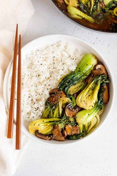 a white bowl filled with rice and vegetables next to chopsticks on a table