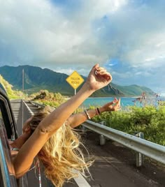 a woman leaning out the window of a car with her hand up in the air