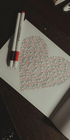 a heart made out of letters on top of a piece of paper next to a pen