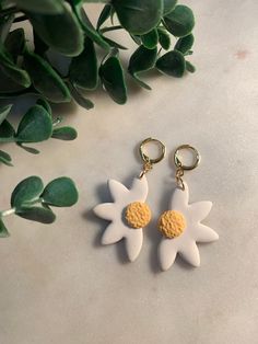 two white and yellow flower shaped earrings sitting on top of a table next to a plant