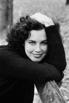 a black and white photo of a woman leaning on a fence smiling at the camera