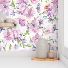 a white vase sitting on top of a counter next to a wallpaper covered in flowers