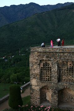 some people standing on top of a stone building with mountains in the background and trees