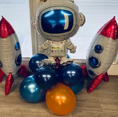 an astronaut balloon sitting on top of balloons in front of a window with two rockets