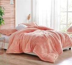 a bed covered in a pink fluffy blanket next to a potted plant on a wooden floor