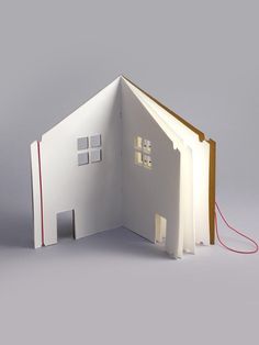 an open book with a house cut out on the inside and red string attached to it