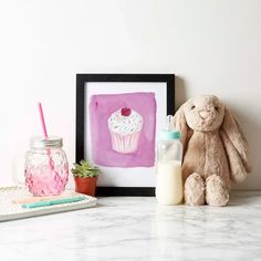 a stuffed animal sitting next to a cupcake on a table with a drink in front of it