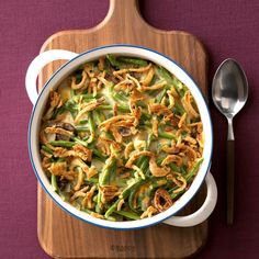 a casserole dish with green beans and onions on a cutting board next to a spoon