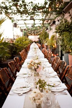 a long table is set up with white flowers and greenery for an outdoor event