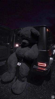 a large black teddy bear sitting in the back of a truck with its lights on