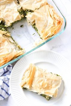 a white plate with a piece of spinach and cheese pie on it next to a glass casserole dish