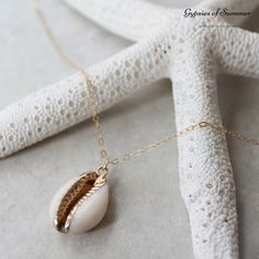 The cowrie seashell necklace will help you embrace the mermaid within even out of water. Combining a dainty chain with a natural white cowrie shell featuring gold details this necklace is ready for you to wear and carry around the beach with you. Layer it with some simple gold chains or alone for a unique standout look. Ideal for the beach lover who has everything. > Natural white cowrie Seashell electroplated in Gold measuring approx. 2cm x 1.5cm (0.79" x 0.60" / 20mm x 15mm) > Genuine 14k Gold Gold Shell Necklace With Starfish Charm On Strand, Gold Shell-shaped Jewelry With Starfish Charm, Shell-shaped Ocean-inspired Jewelry With Starfish Charm, Gold Shell-shaped Necklace With Starfish Charm, Ocean-inspired Jewelry With Starfish Charm And Shell Shape, Gold Necklace With Starfish Charm, Ocean-inspired Shell Jewelry With Starfish Charm, Shell Necklaces With Starfish Charm, White Shell-shaped Jewelry With Starfish Charm