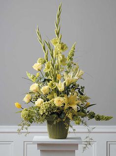 a green vase filled with yellow flowers on top of a white tablecloth covered floor