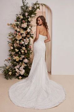 a woman in a white wedding dress standing next to a flower covered wall with flowers on it