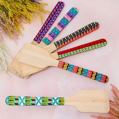 wooden spoons with colorful beaded handles on a pink surface next to dried flowers