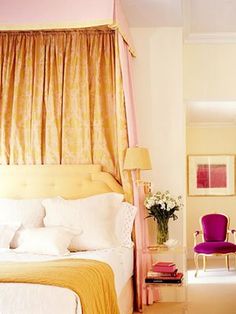 a bedroom with yellow and white bedding, pink chair, and window drapes