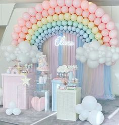 a table topped with balloons and cake next to a rainbow shaped arch covered in pastel colors