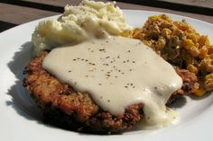 a white plate topped with meat covered in gravy and mashed potatoes