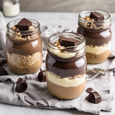 three jars filled with desserts sitting on top of a white cloth next to spoons