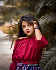 a woman in red top and striped skirt posing for the camera with palm trees behind her