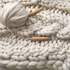 two knitting needles are on top of a white knitted blanket with yarn and wood pins