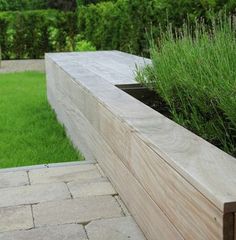 a wooden planter sitting in the middle of a lush green field next to a stone walkway