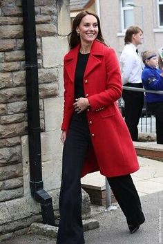 a woman in a red coat and black pants is walking down the street with her hand on her hip