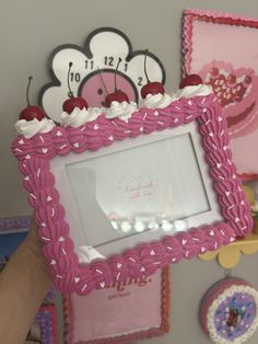 a person holding up a cake shaped like a photo frame with cherries on it