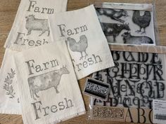 four farm tea towels on top of a wooden table next to stamp pads and rubber stamps