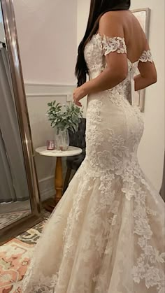 a woman in a wedding dress looking at herself in the mirror with her hand on her hip