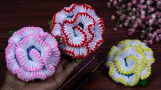 three crocheted flowers sitting on top of a wooden table next to knitting needles